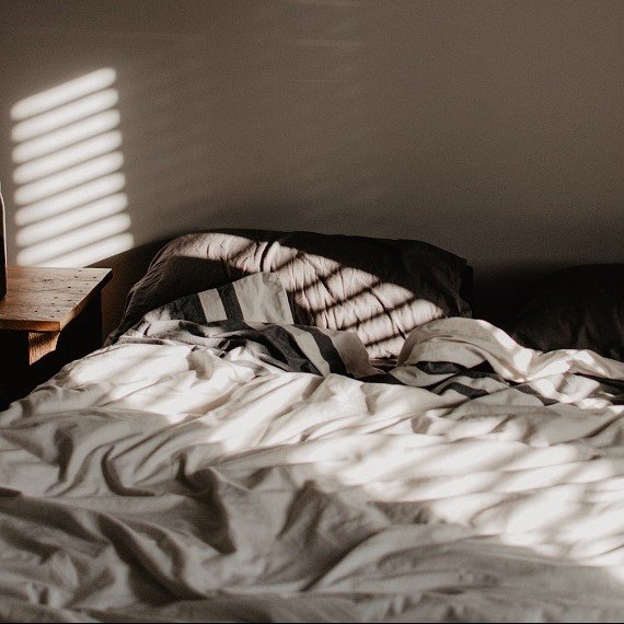 Bed sheets and pillows in sunlight room filtered through venetian blinds_Sally-Annes Story